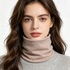 A woman with long dark hair wearing a beige turtleneck sweater and a matching neck warmer scarf.