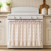 A white farmhouse oven skirt with a floral pattern and ruffle trim installed on a white stove.