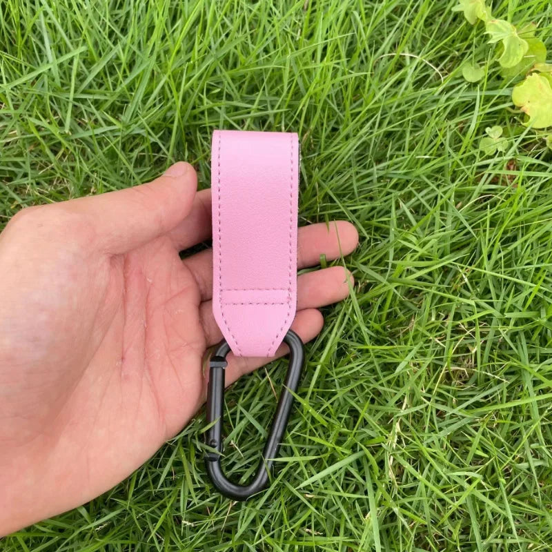 A hand holds a pink PU leather baby bag organizer with a hook for a stroller.