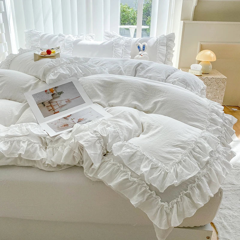 A white ruffled duvet cover set with pillows and a matching pillow is displayed on a bed in a bright room.