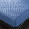 A close-up view of a blue quilted waterproof mattress protector with deep pockets resting on a black surface.