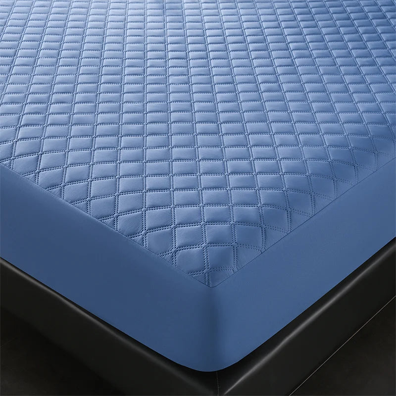 A close-up view of a blue quilted waterproof mattress protector with deep pockets resting on a black surface.
