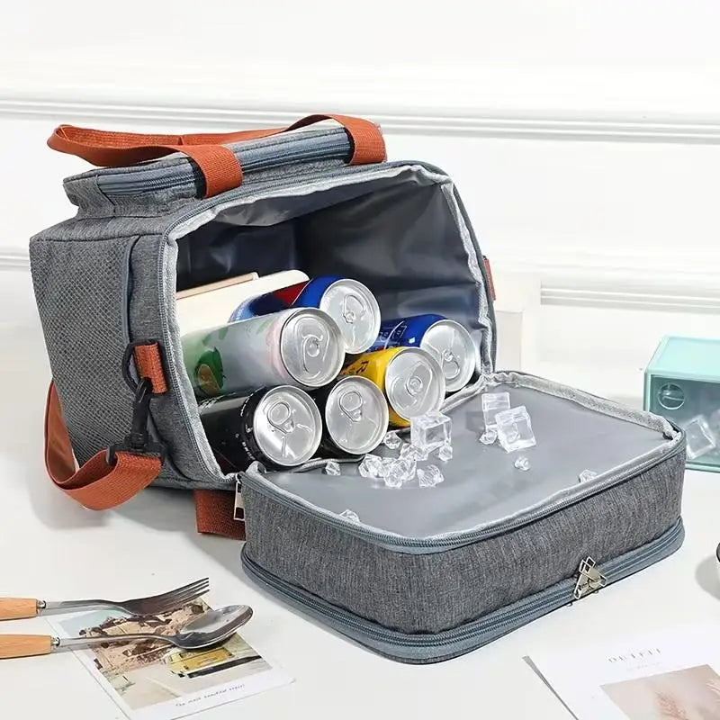 A gray insulated lunch bag is open, showing a clear double-layer compartment with various food items and ice cubes.