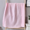 A pink, textured muslin cotton blanket hanging on a wooden hanger against a gray wall.