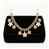 A black clutch bag with a gold chain and pink flower charms attached.