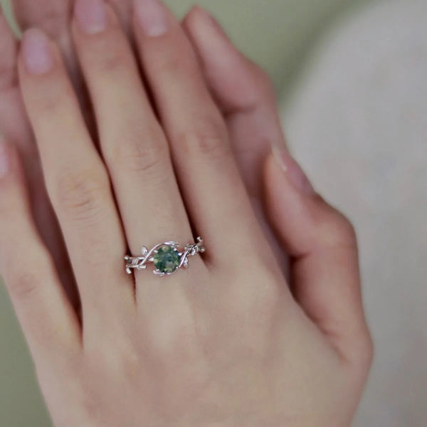 Primer plano de una mano con un anillo de moscagita de plata esterlina con delicados detalles de vid en plata.