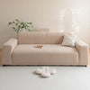 A light beige plush sofa cover with a white decorative pillow and a small bowl on a white rug.