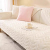 A pink cushion on a white quilted sofa with a white mat in a bright room.