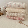 Stack of floral muslin baby blankets in soft pink and cream tones