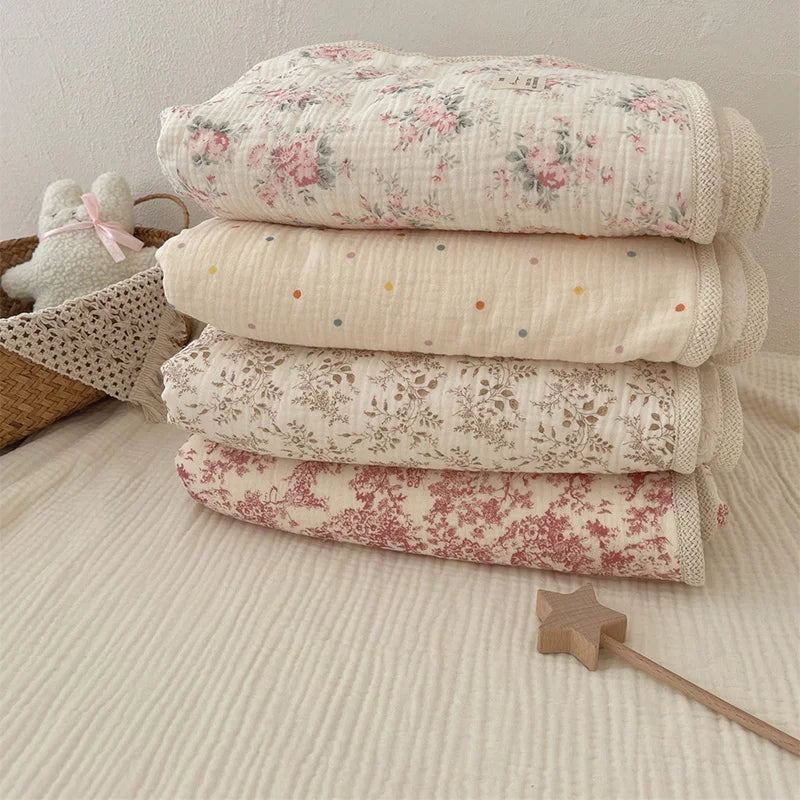 Stack of floral muslin baby blankets in soft pink and cream tones