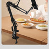 A black adjustable phone stand with an overhead light is positioned above a table with food and drinks, demonstrating multi-d