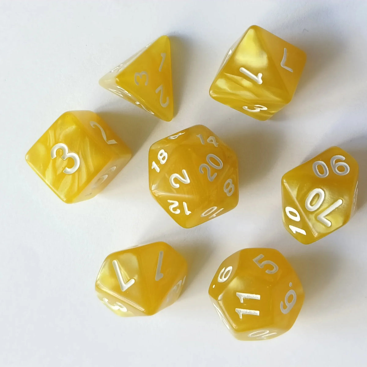 A collection of seven yellow translucent polyhedral dice arranged on a white surface.