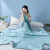 Light blue cooling summer quilt draped on a bed with white pillows and a light blue wall.