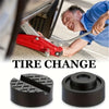 A close-up of a person performing a tire change using a red floor jack and rubber pad on the ground.