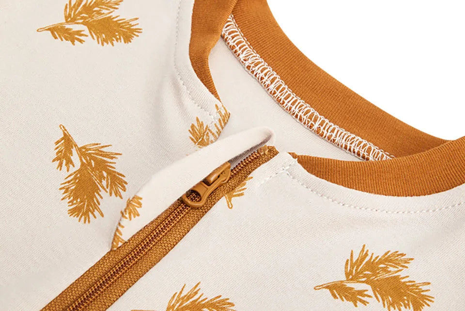 Close-up of a white baby sleep sack with gold leaf pattern and a tan zipper detail.
