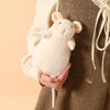 A small, fluffy white rabbit plush toy is being held by a hand against a brown fabric background.