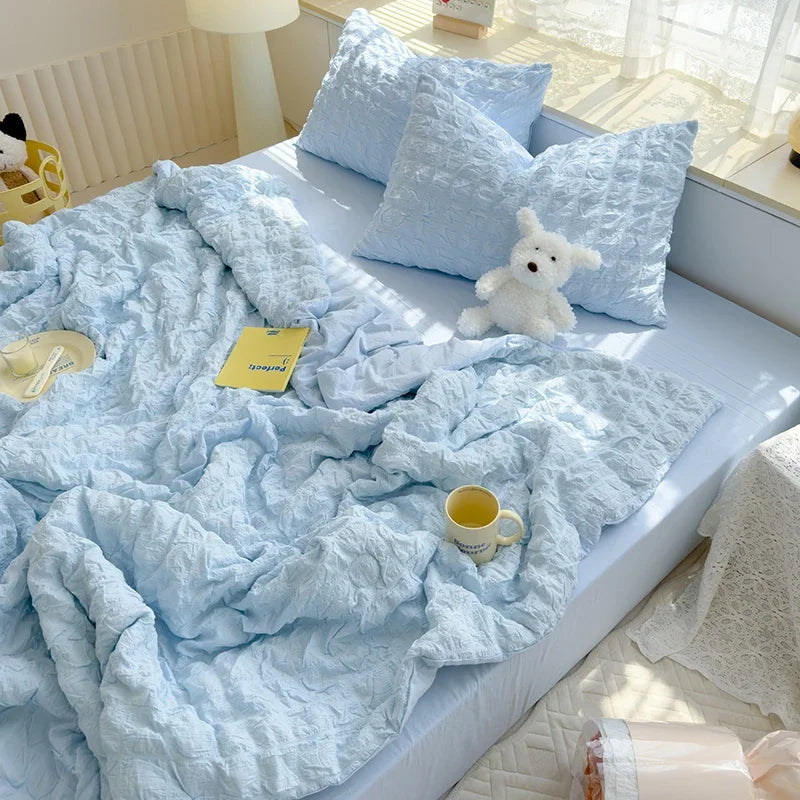 Light blue breathable summer seersucker quilt with white pillows and a yellow tag on a bed