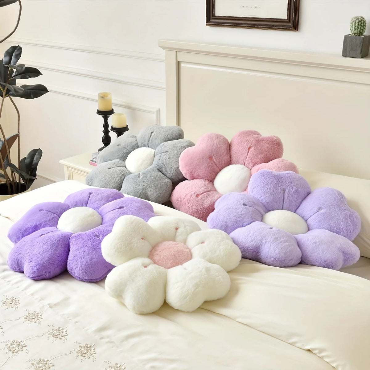 A collection of plush daisy flower throw pillows in shades of purple, pink, and gray resting on a white bed.