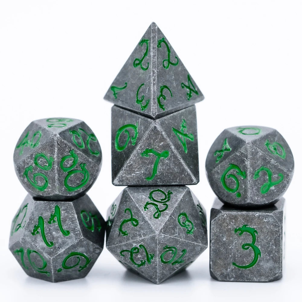 A set of seven metal polyhedral dice in gray with green dragon font designs, including a pyramid and cube shapes.