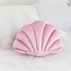 A pink velvet decorative shell print throw pillow resting on a white textured surface.