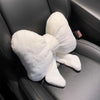 A white plush bowknot car headrest pillow with neck support resting on a dark gray car seat.