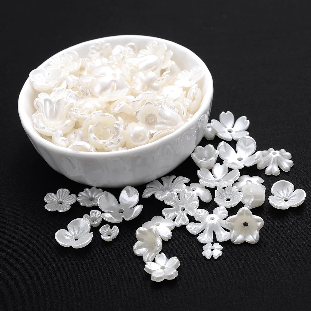 A white bowl filled with acrylic pearl spacer beads and loose floral-shaped beads on a dark background.