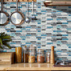 A kitchen backsplash featuring blue, gray, and white tile stickers mounted on a wooden shelf above a light wood countertop.