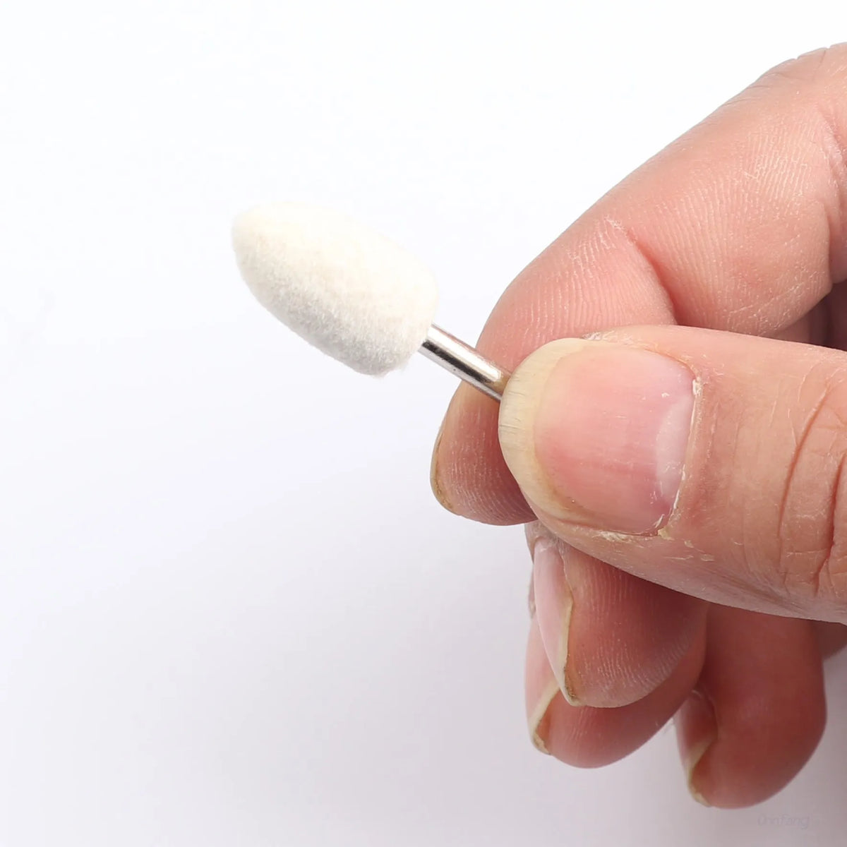 A hand holds a white wool felt polishing wheel with a metal shank for rotary tools.