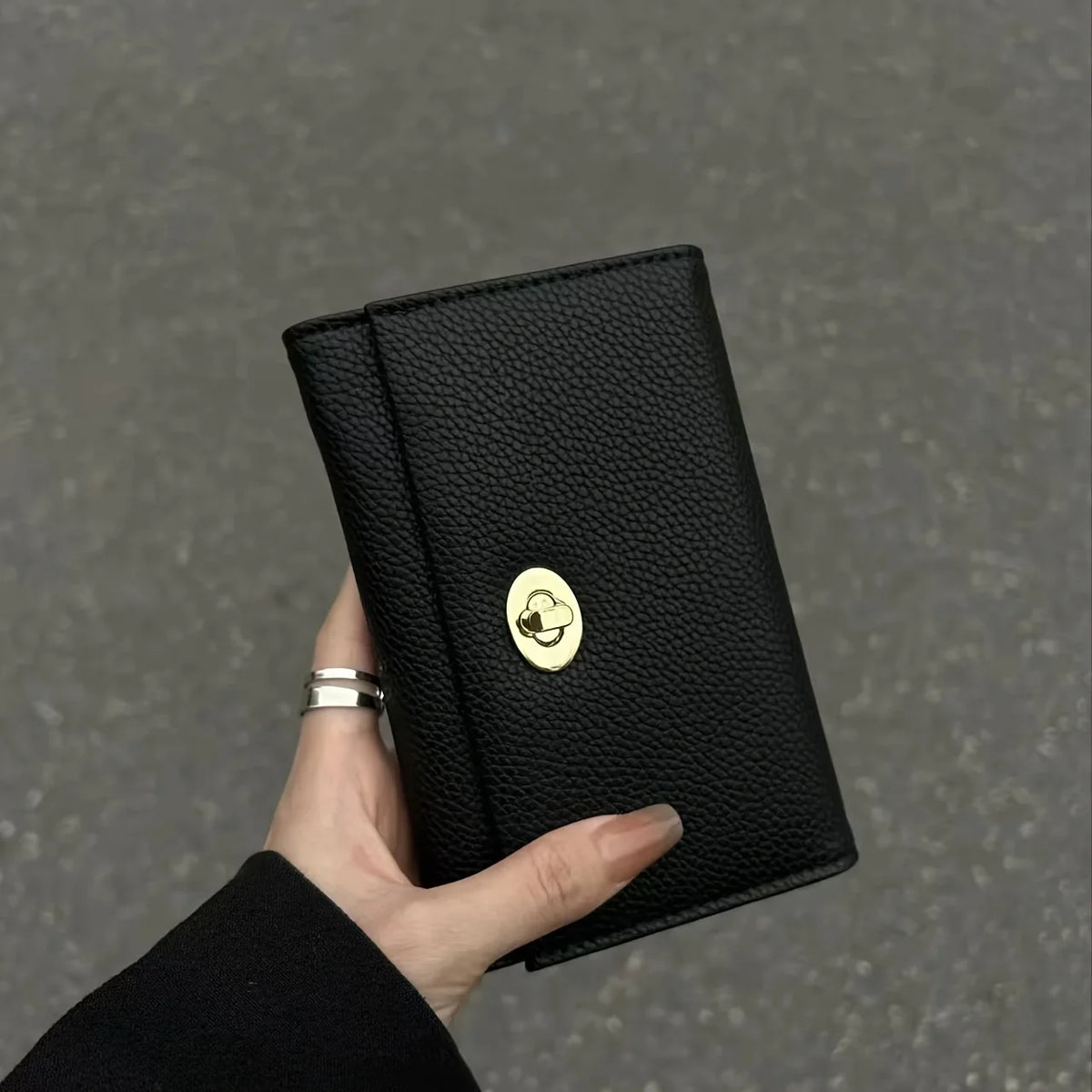 A hand holds a sleek black compact wallet featuring a gold cloud emblem.