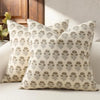 A close-up of a beige throw pillow cover with a repeating gray floral pattern resting on a white sofa.