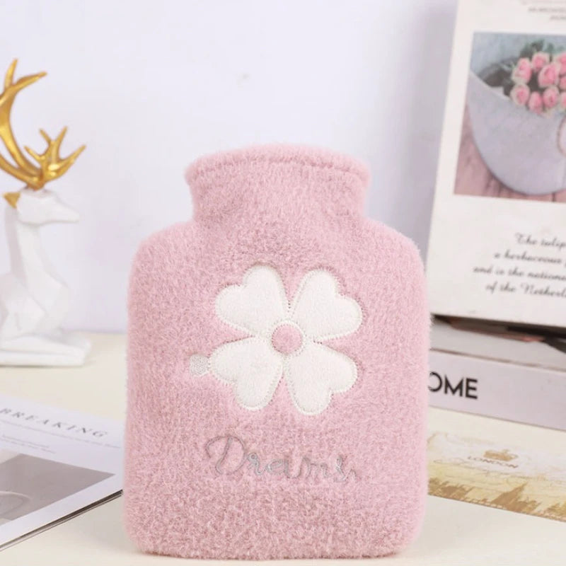 A pink plush-covered hot water bottle with a white flower design and the word Dreams on it.