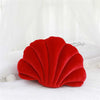 A vibrant red velvet decorative shell print throw pillow resting on white bedding.