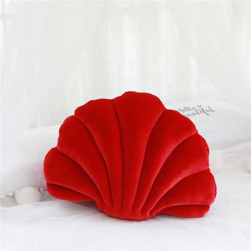 A vibrant red velvet decorative shell print throw pillow resting on white bedding.