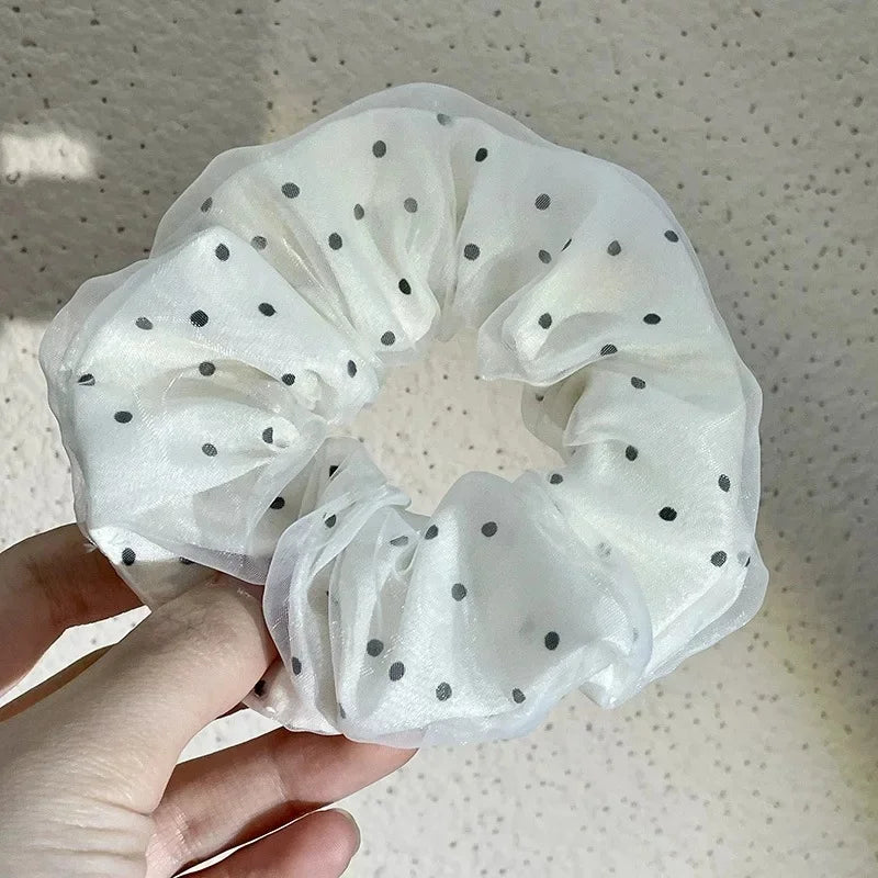 A white polka dot mesh scrunchie hair tie is being held by a hand against a light background.