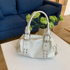 A white soft PU leather shoulder bag with silver rivet accents resting on a white table.