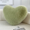 A fluffy, light green heart-shaped throw pillow resting on a white sofa.