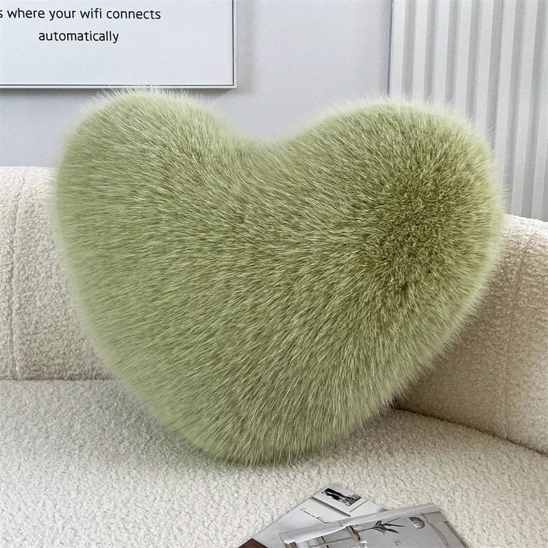A fluffy, light green heart-shaped throw pillow resting on a white sofa.