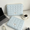 A light blue quilted laptop sleeve with a soft lining resting on a white surface next to a silver laptop and sunglasses.