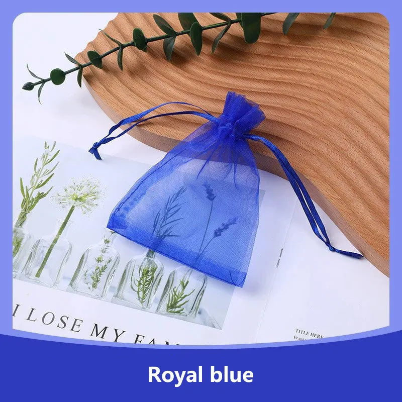 A royal blue organza drawstring gift bag filled with dried herbs, resting on a wooden surface.