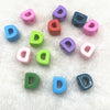 A collection of ten mixed colored alphabet letter beads scattered on a white, fluffy surface.