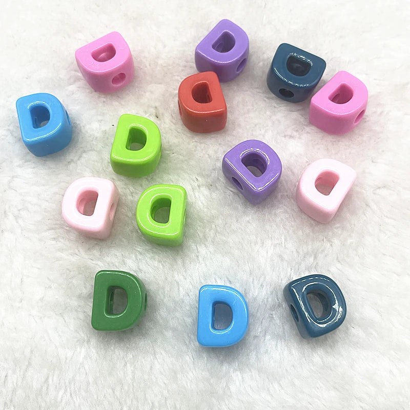 A collection of ten mixed colored alphabet letter beads scattered on a white, fluffy surface.