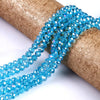 A strand of bright blue faceted crystal glass spacer beads is coiled on a brown cylindrical object.