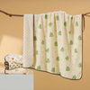 A cream-colored cotton gauze baby swaddle blanket with a bear print pattern is hanging on a wooden branch.