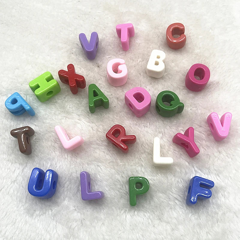 A collection of 10 mixed alphabet letter beads in various colors like purple, green, red, and pink scattered on a white surfa