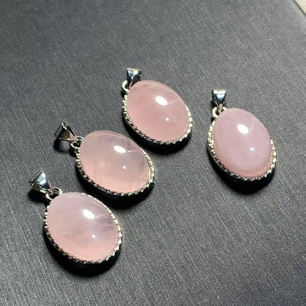 Un ensemble de colliers pendants ovales en quartz rose naturel avec finitions en argent, présentés sur une surface sombre.
