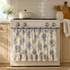 A white farmhouse oven skirt with a floral pattern and ruffle trim is installed on a stove.
