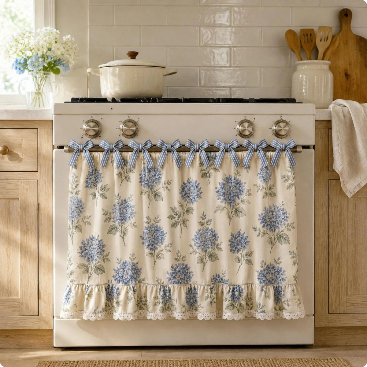 A white farmhouse oven skirt with a floral pattern and ruffle trim is installed on a stove.
