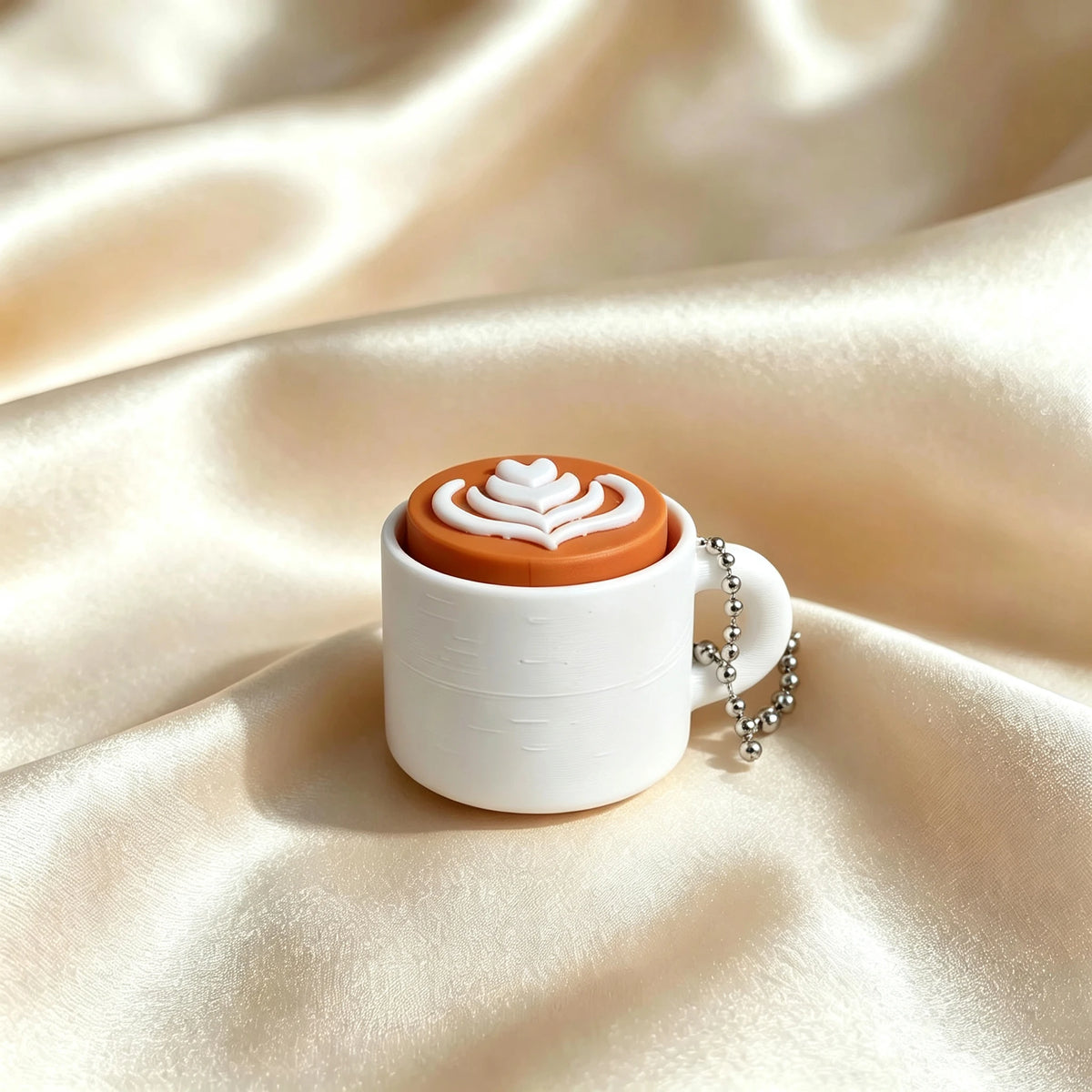 A white mug with an orange lid featuring a white heart design and a silver chain keychain, set against a silky beige backgrou