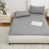 A gray waterproof mattress protector with elastic straps is placed on a bed, featuring a quilted top and a white label.