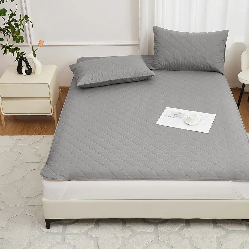 A gray waterproof mattress protector with elastic straps is placed on a bed, featuring a quilted top and a white label.